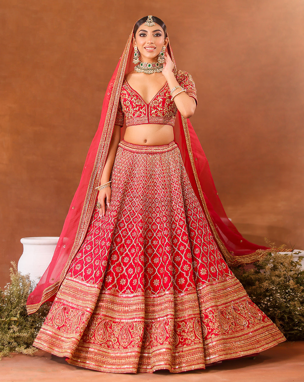 A woman models a deep rosewood bridal lehenga set with intricate gold embroidery.