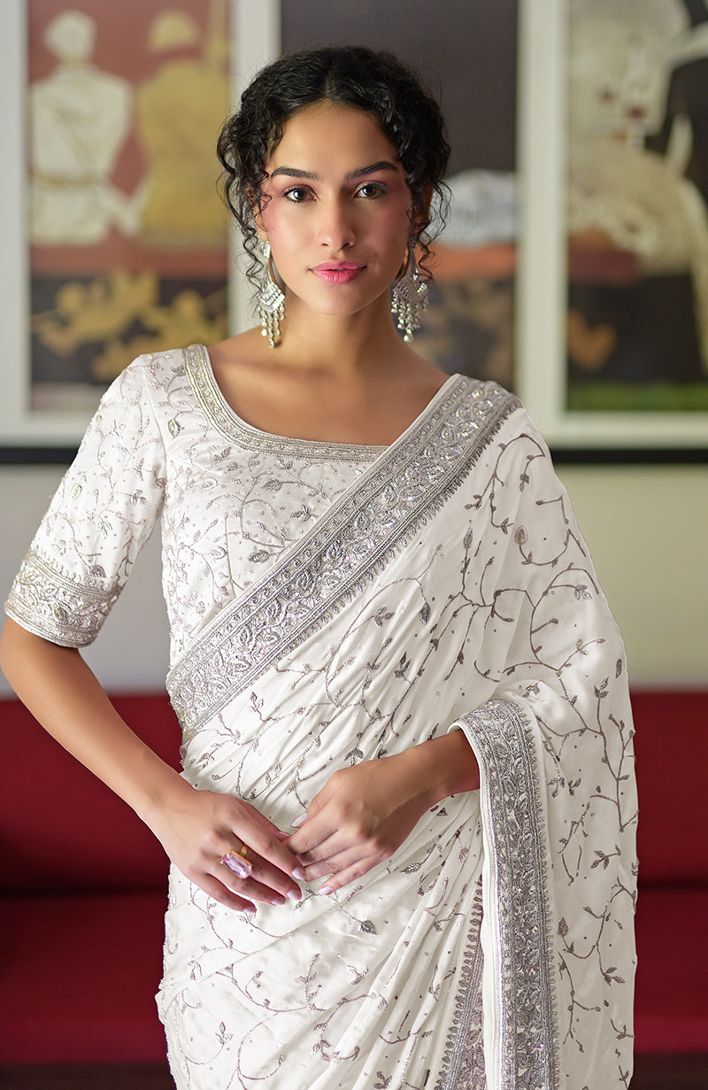A woman in a white silk saree with silver embroidery and a matching blouse.