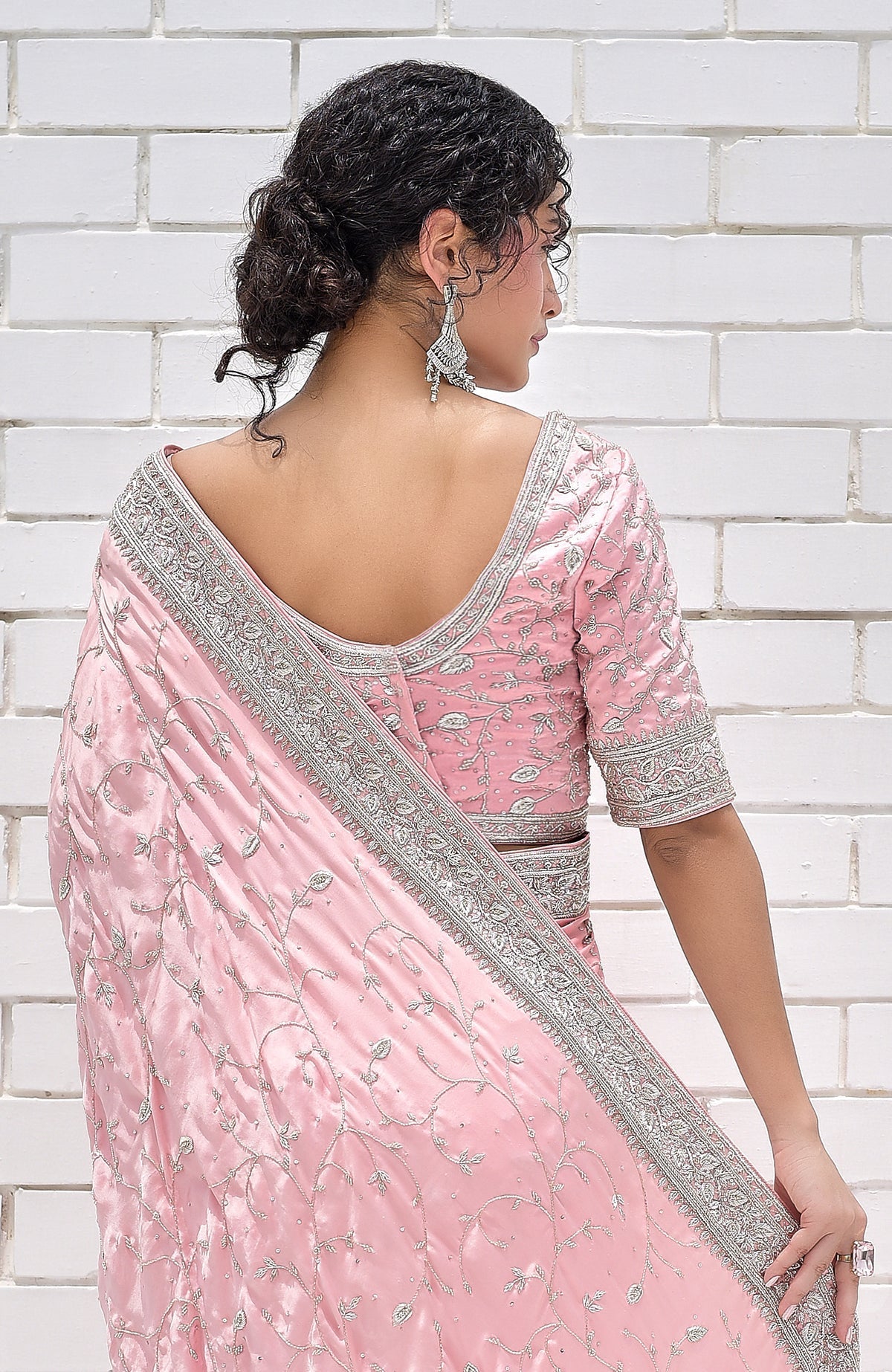A woman from the back wearing a pink pure silk saree with silver zardozi embroidery.