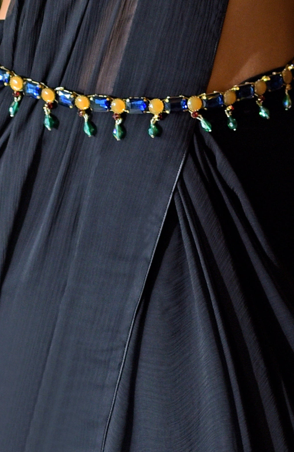 Black chiffon saree with a blue and yellow jeweled belt featuring green dangling stones.