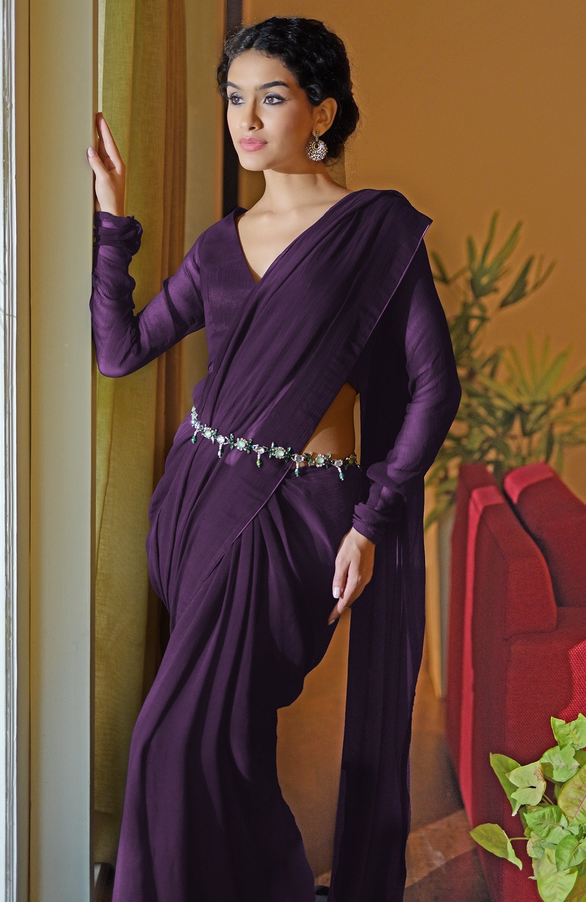 A woman in a purple saree with a V-neck blouse and a jeweled belt.