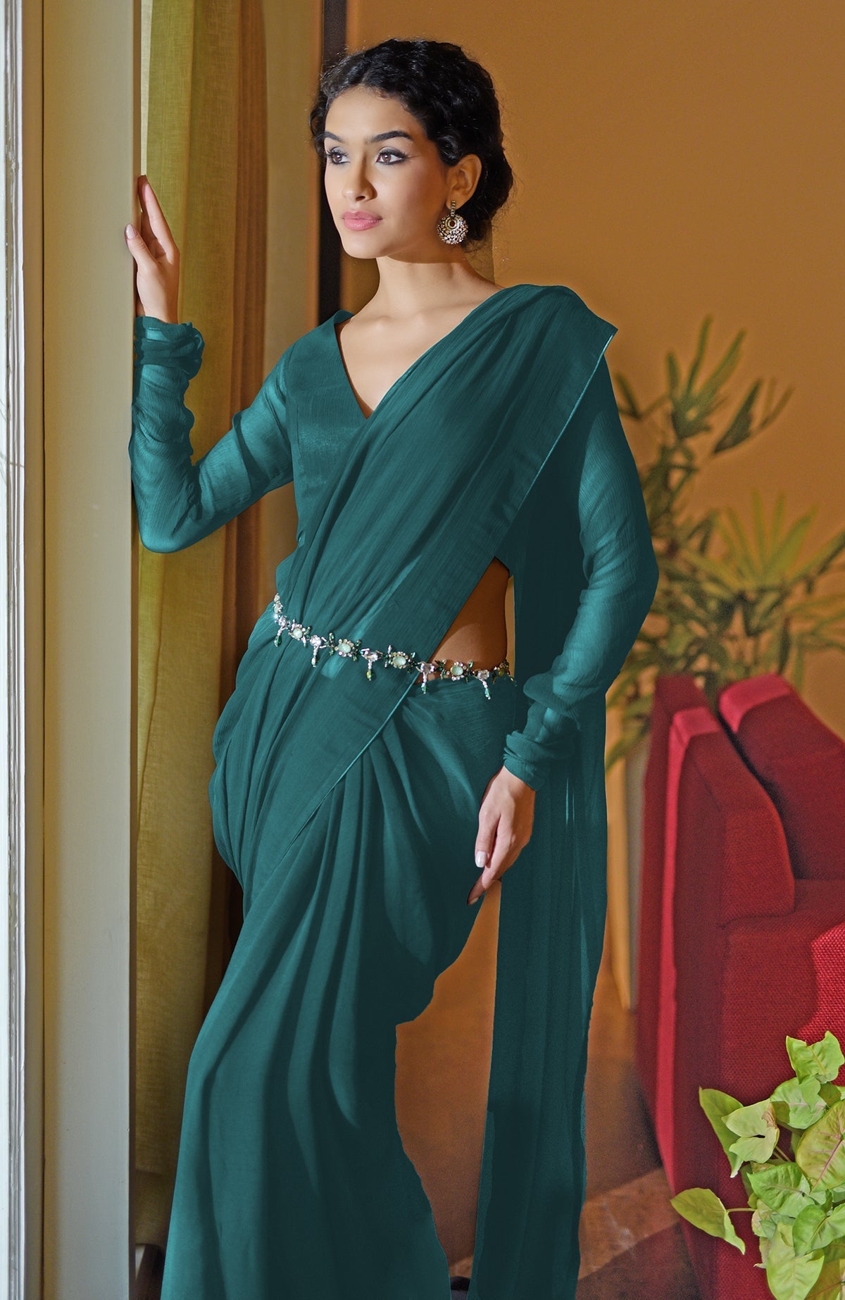 A woman in a teal chiffon saree with a V-neck blouse and a jeweled belt.
