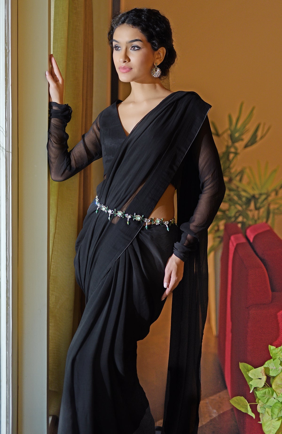 A woman models a classic black chiffon saree with a sheer-sleeved blouse and a jeweled belt.