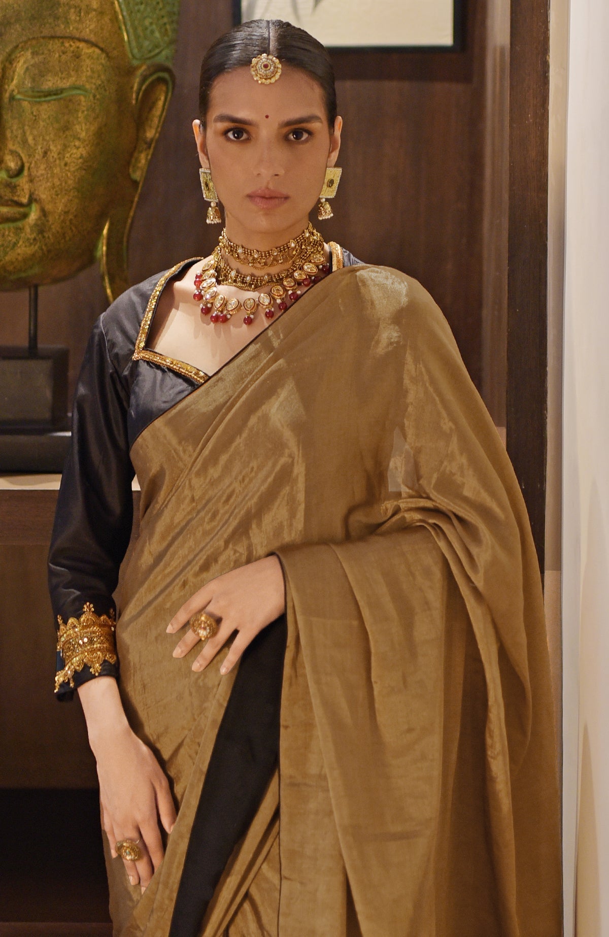 Woman in a gold tissue saree with a black zardozi embroidered blouse.