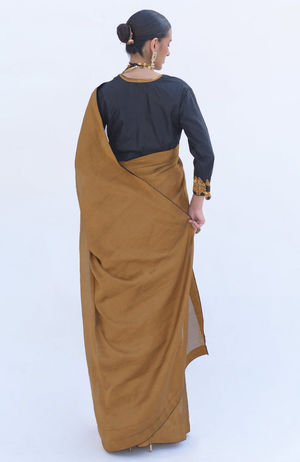 Woman in a gold tissue saree with a black zardozi embroidered blouse.