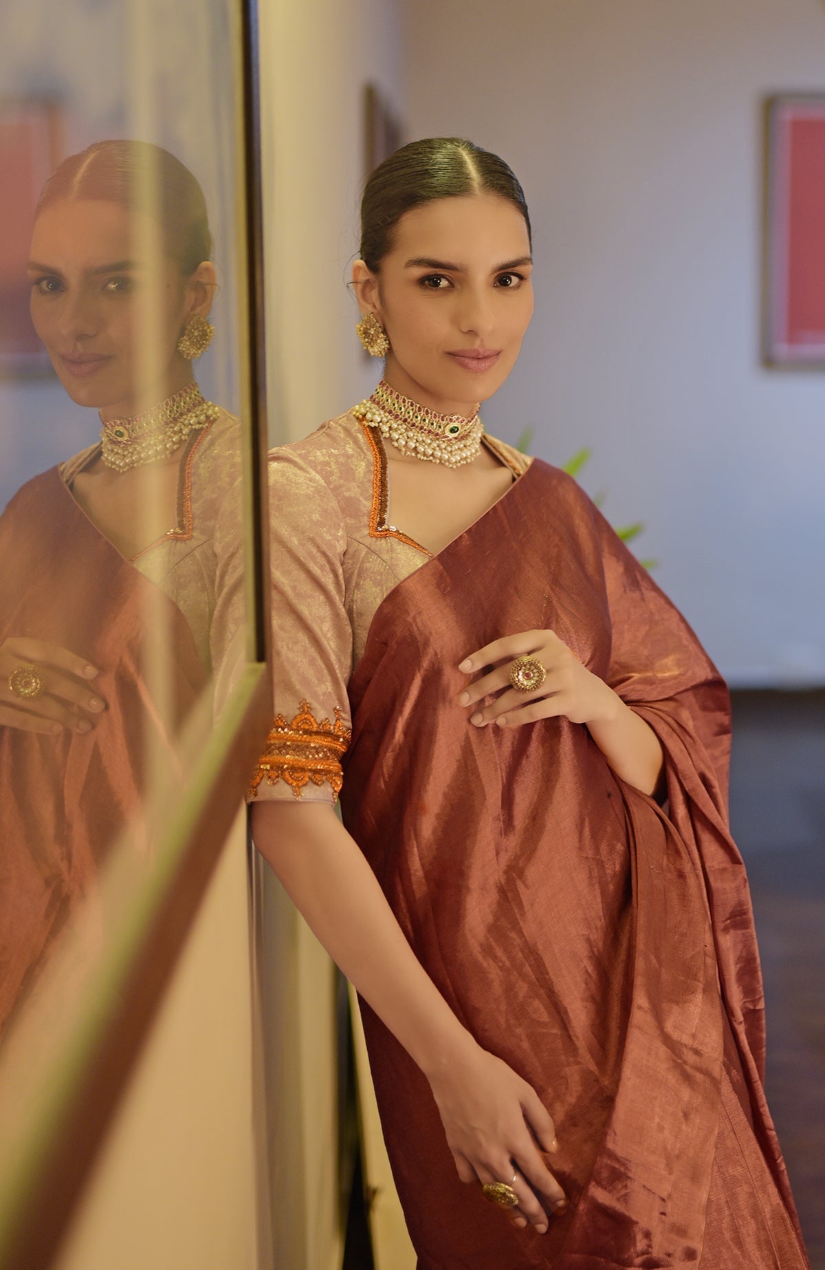 A woman in a copper tissue saree and a pink zardozi embroidered blouse.