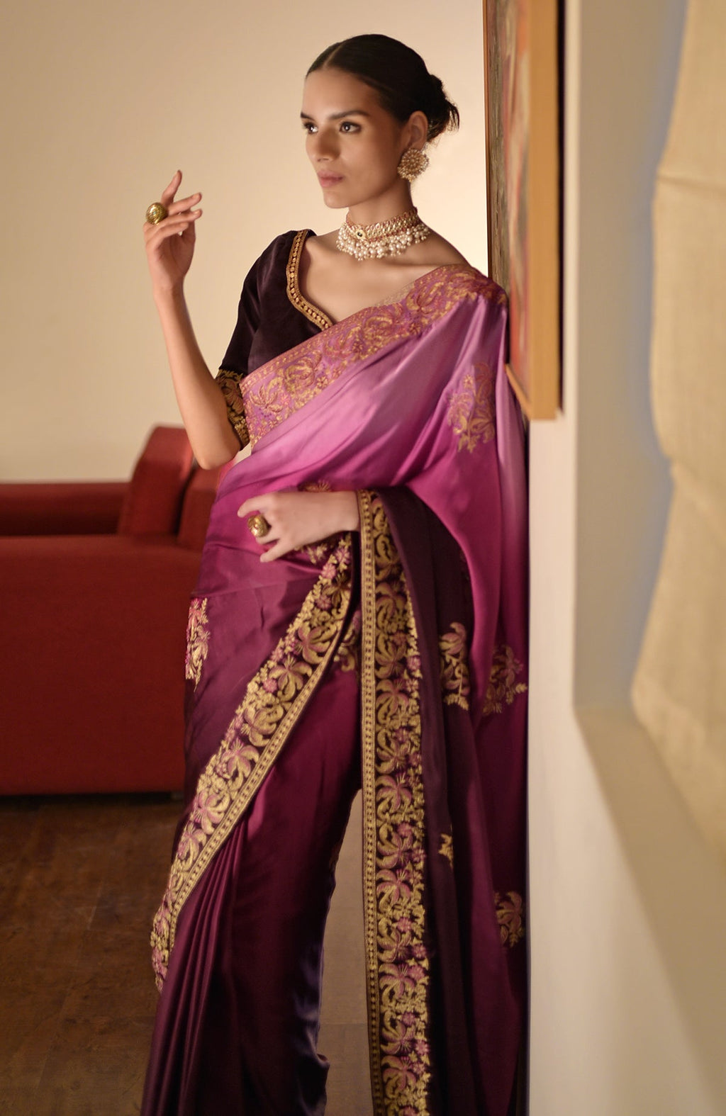 A woman models a wine-pink ombre saree with gold embroidery and a wine blouse.
