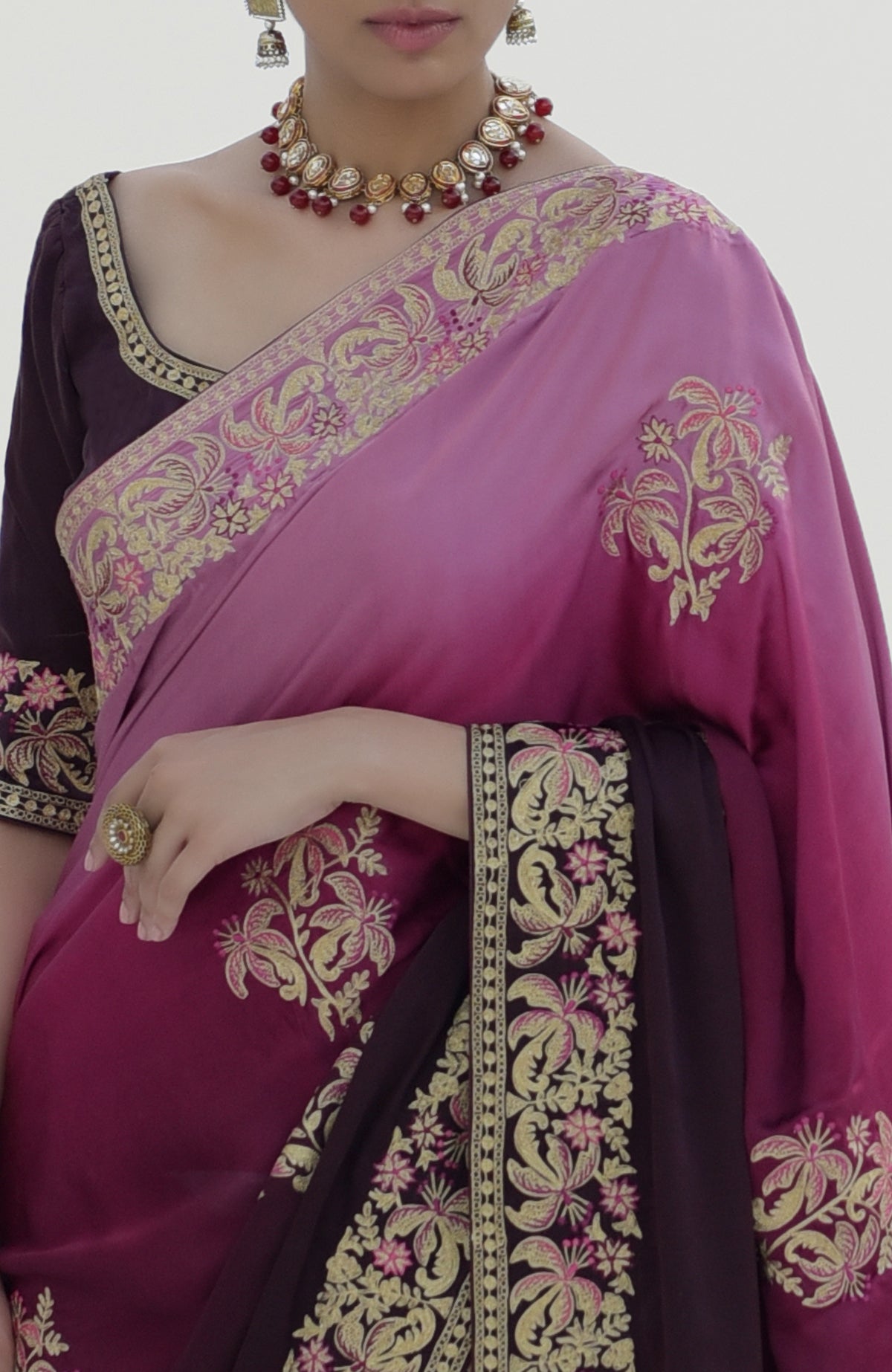 A woman models a wine-pink ombre saree with gold and pink floral embroidery.
