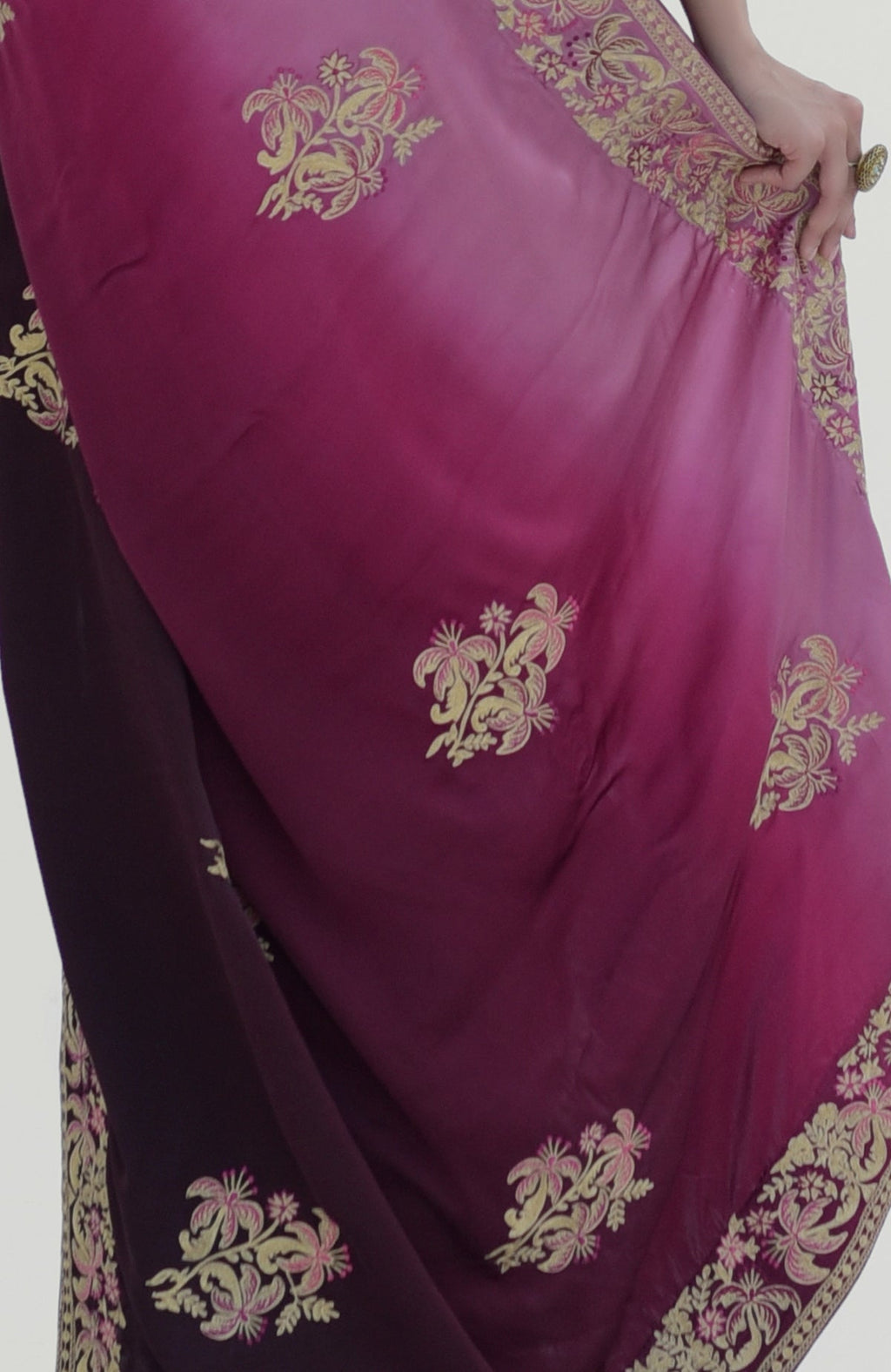 Wine-pink ombre saree with gold Kashidakari embroidery and a hand holding the fabric.