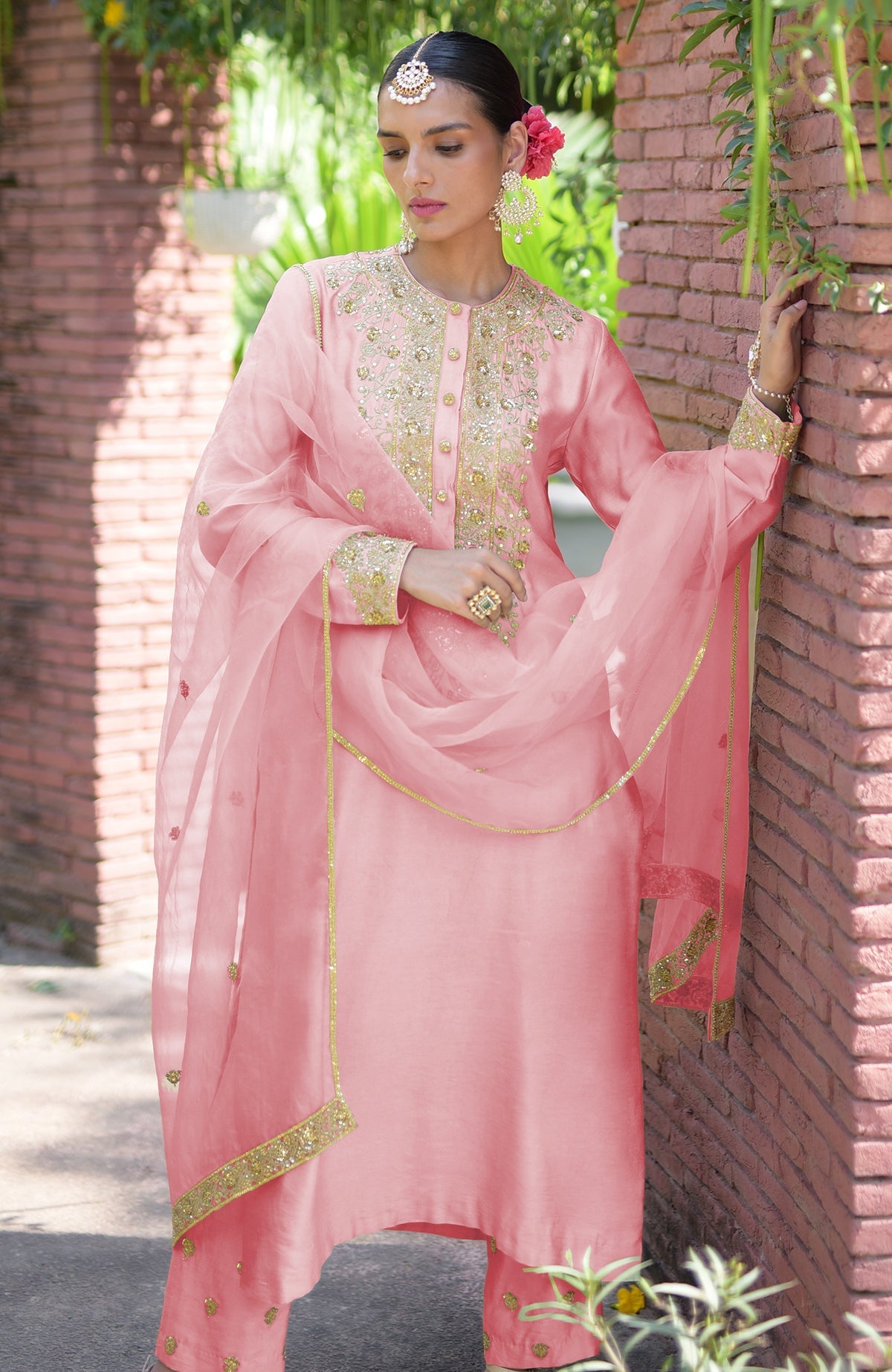 A woman in a pink kurta set with gold embroidery and a sheer dupatta.