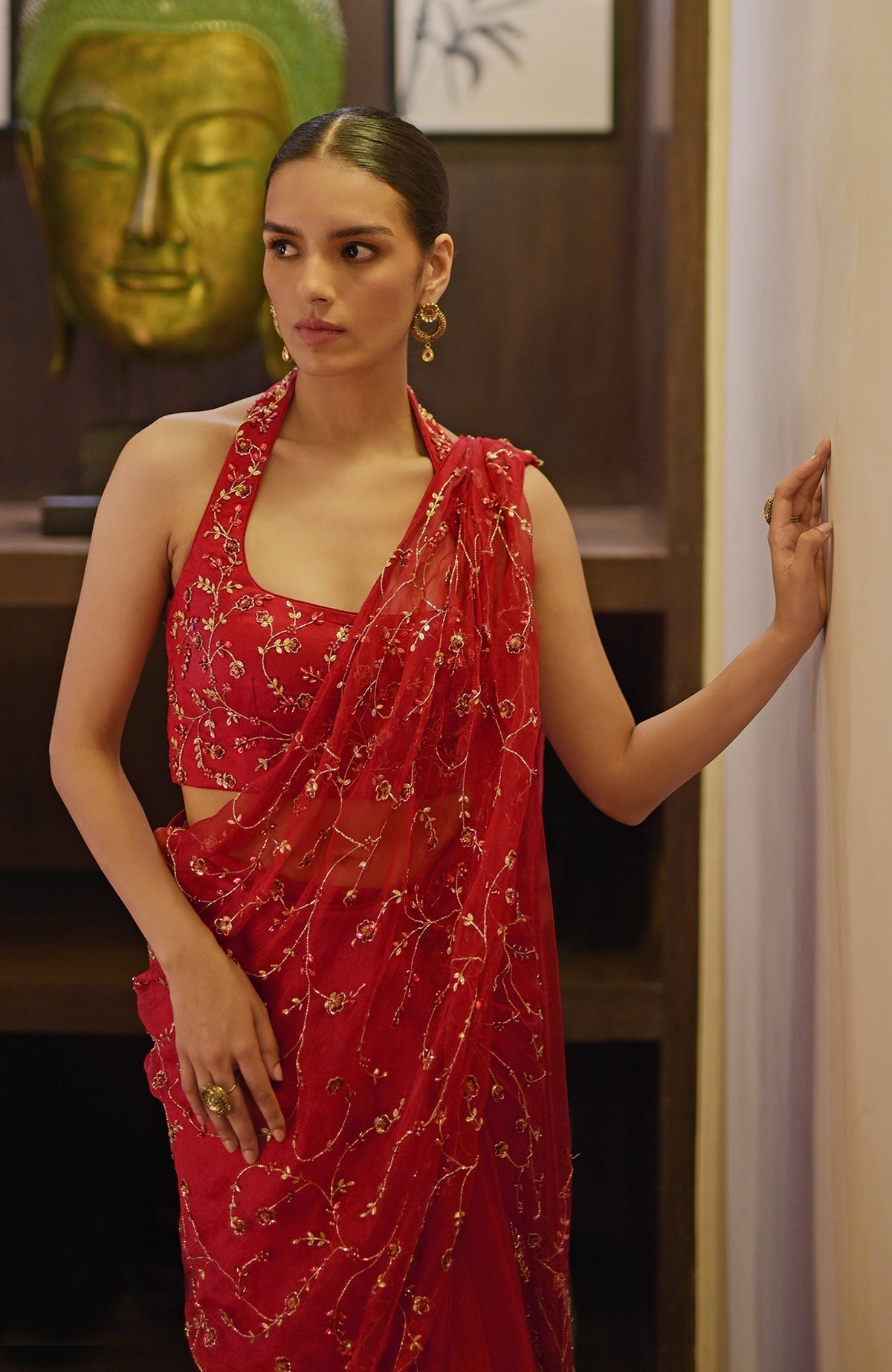 A woman models a red hand-embroidered draped saree set with a halter neck blouse.