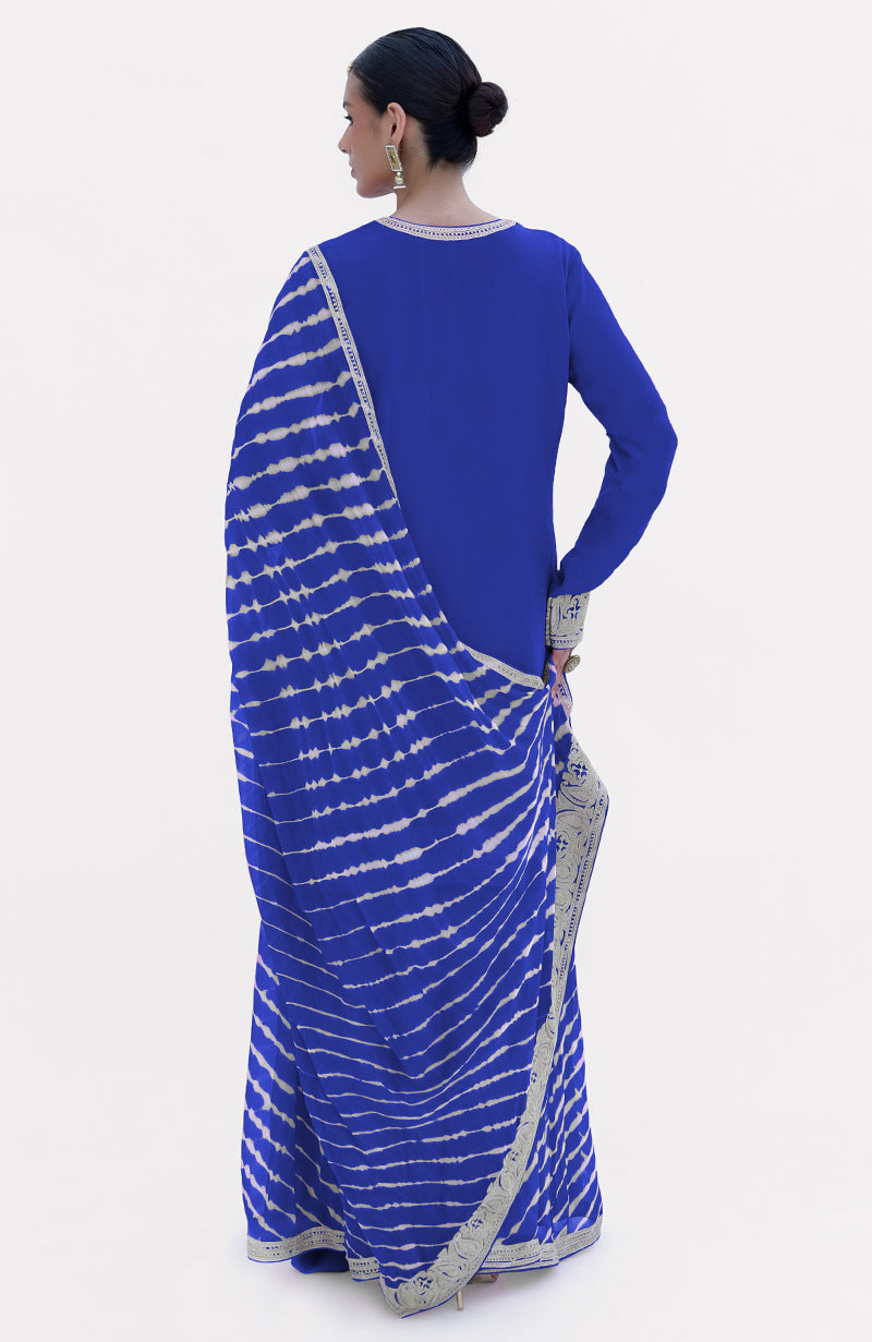 A woman models a royal blue leheriya sharara set with silver tilla embroidery.