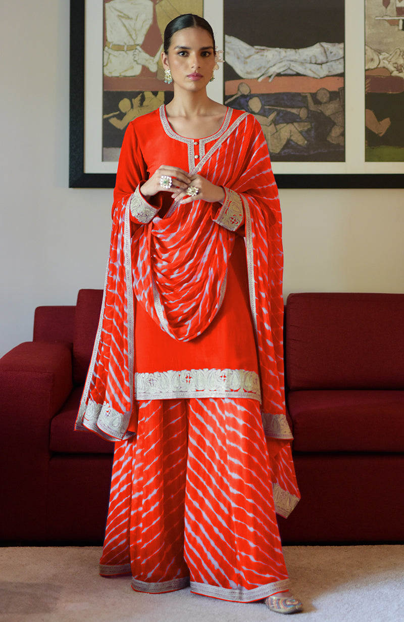 A woman models a red leheriya handcrafted tie-dye and Kashmiri tilla sharara set.