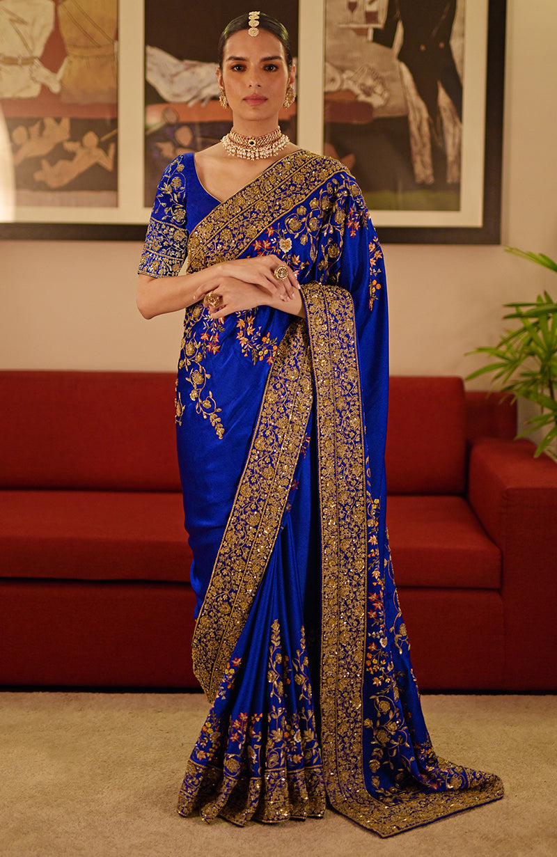 A woman models a blue saree with intricate gold and multi-color embroidery.