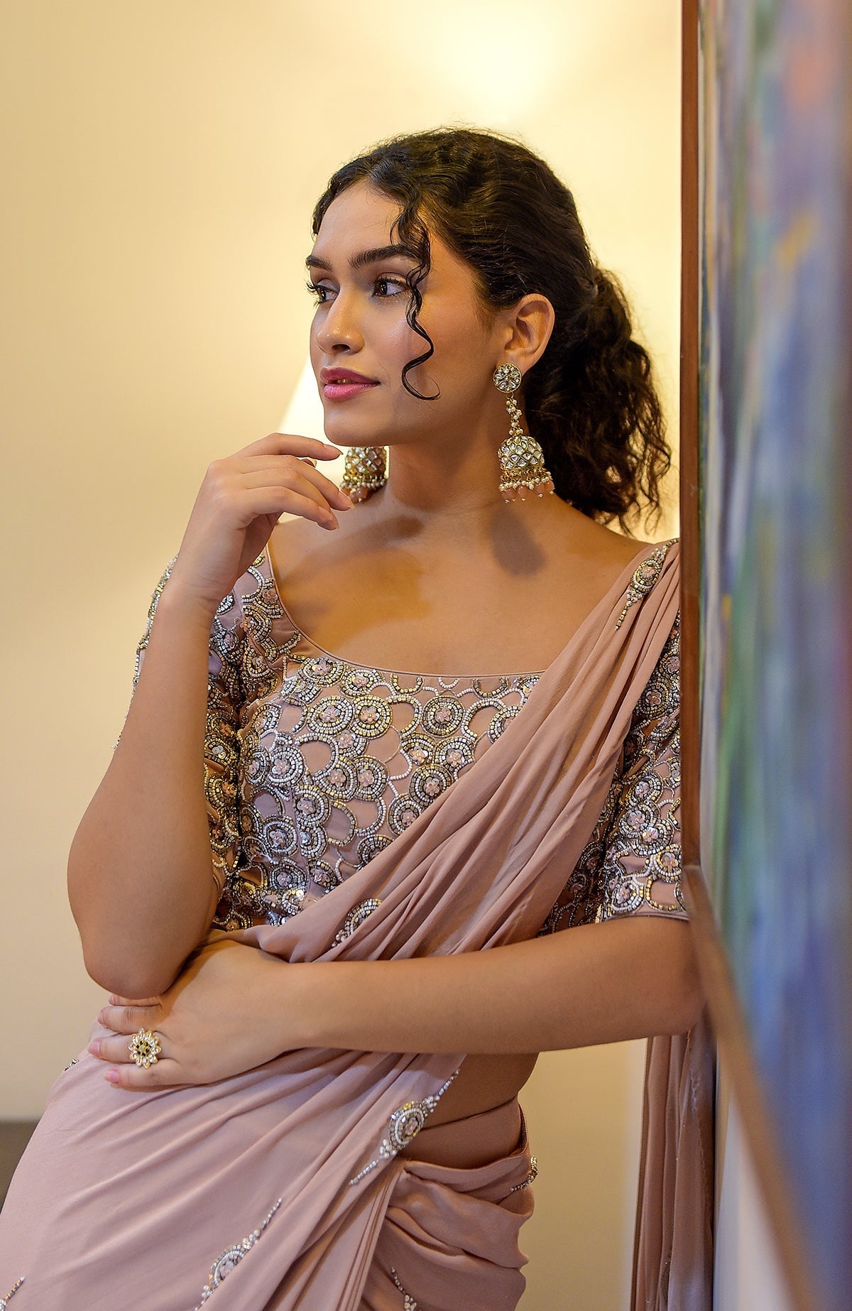 A woman in a nude hand-embroidered pre-draped saree with a matching blouse and large earrings.