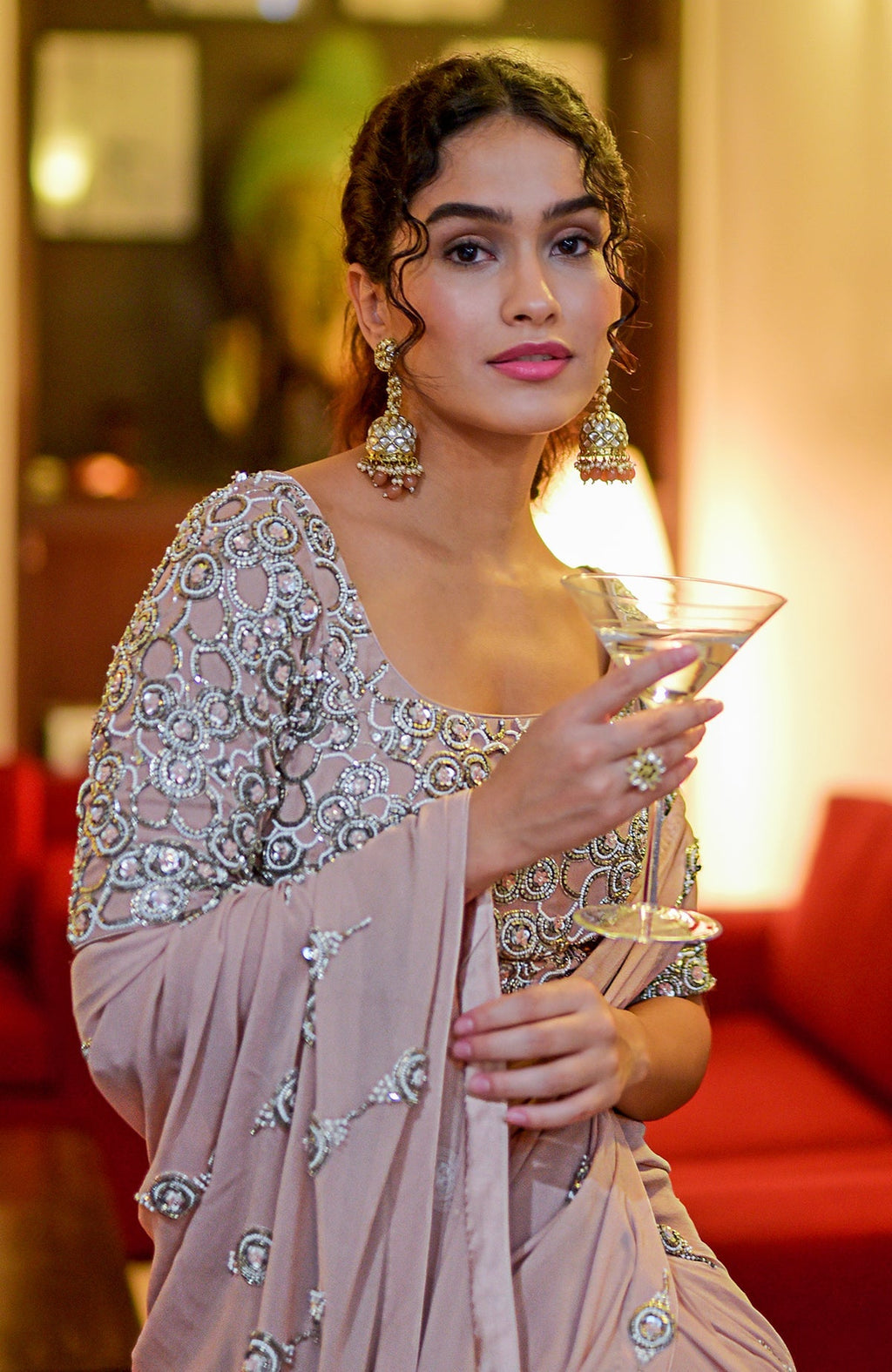 A woman in a nude hand-embroidered pre-draped saree holds a martini glass.