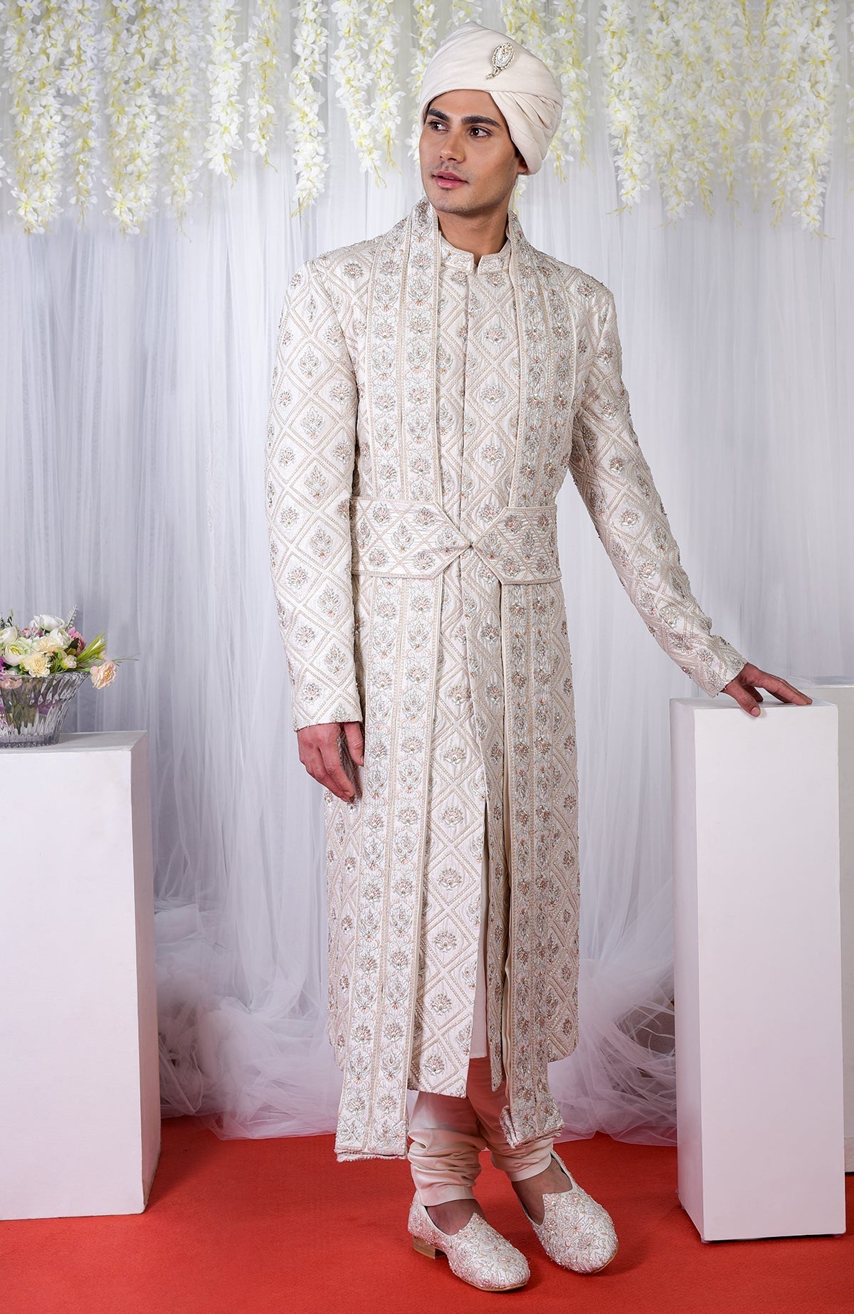 A man models an ivory geometric floral embroidered sherwani set with a matching turban.