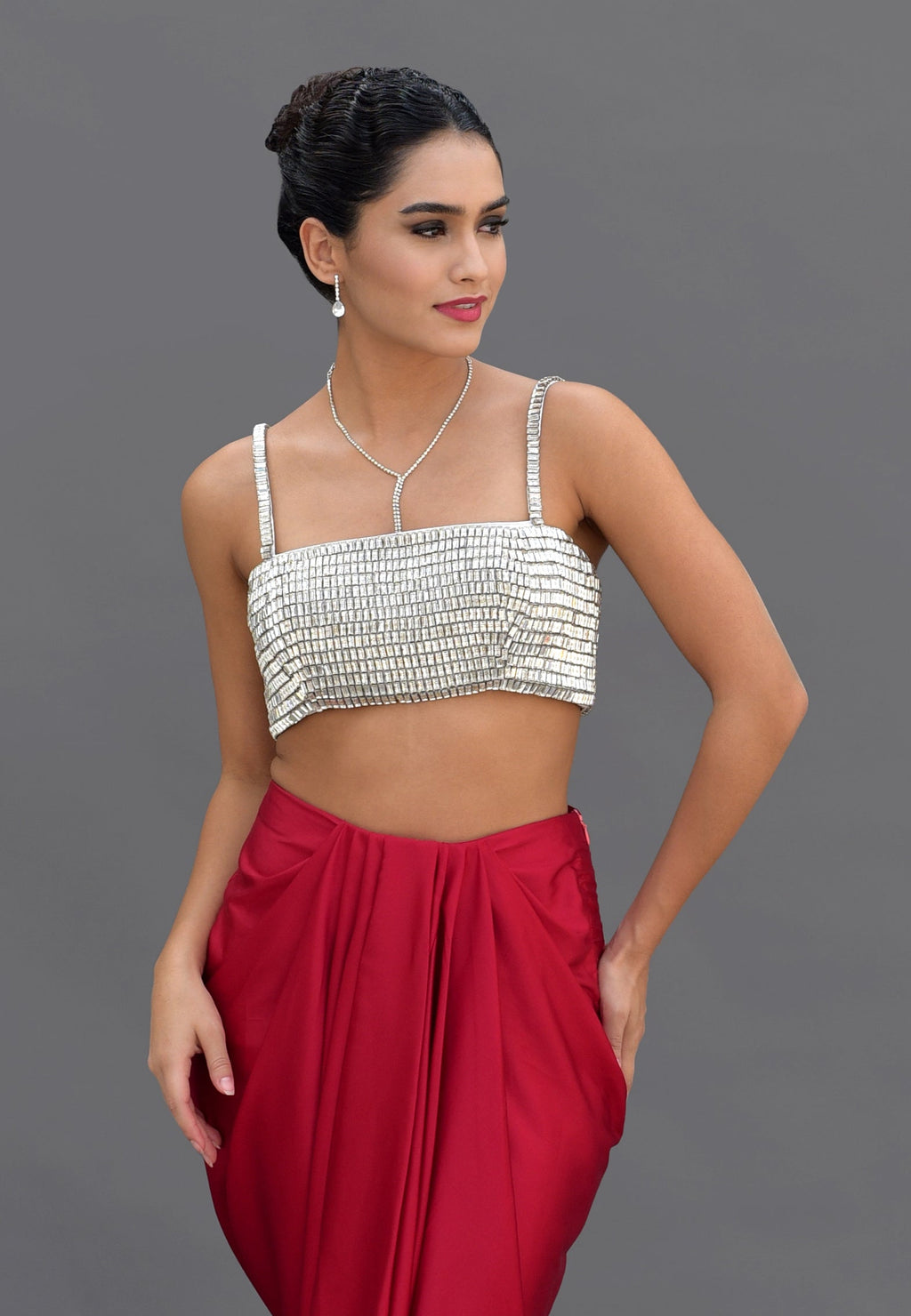 A woman models a silver crystal-embroidered bustier and a red draped skirt.