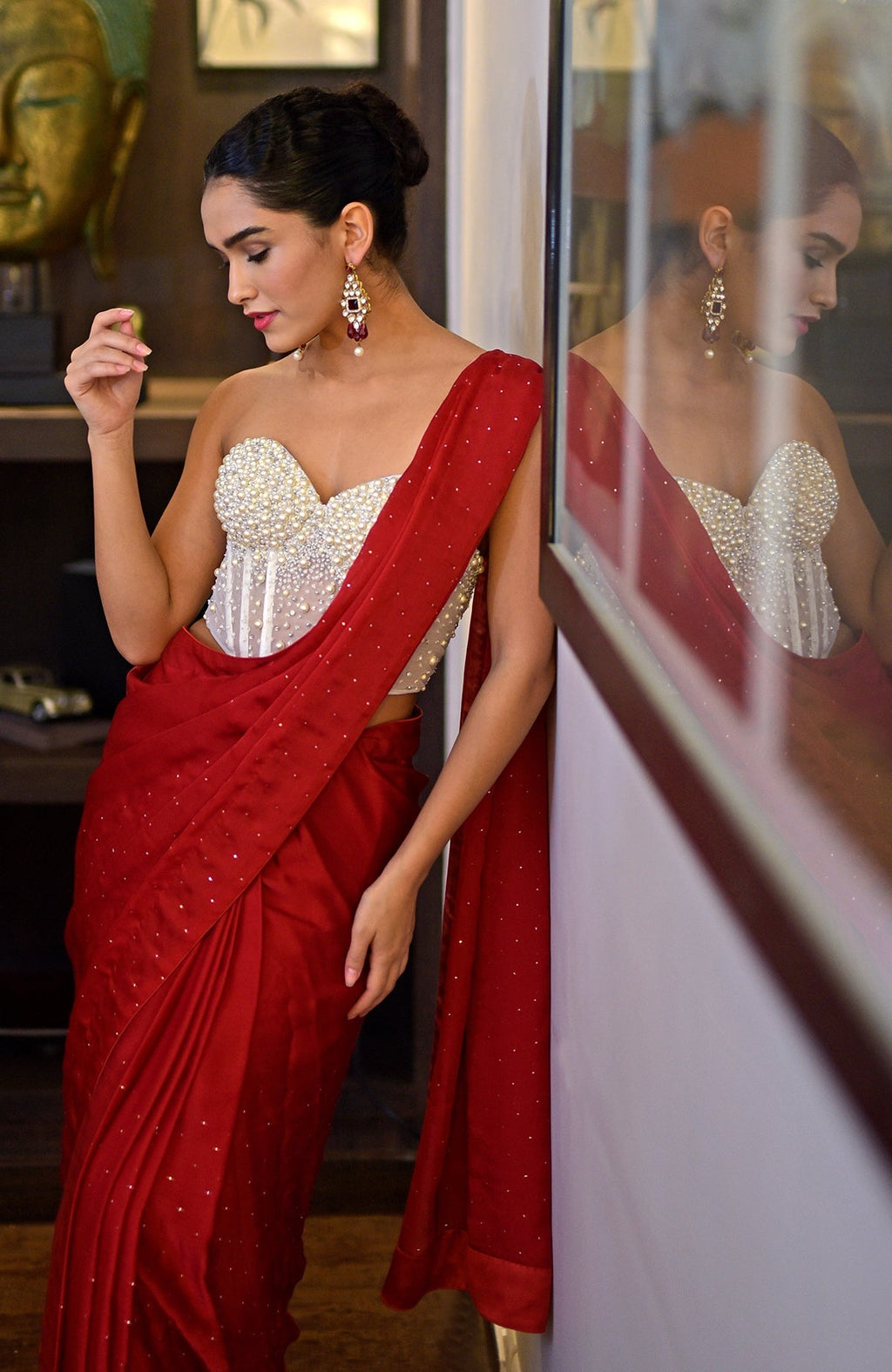 A woman in a white pearl-embroidered corset and a red saree with gold accents.