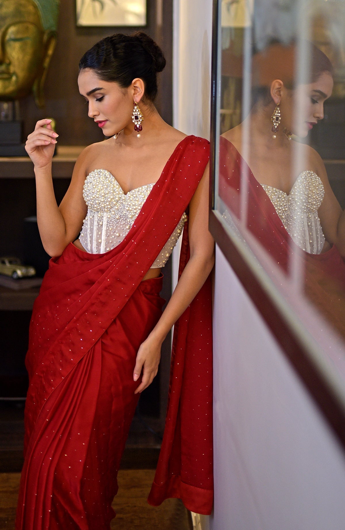A woman in a white pearl-embroidered corset and a red saree with gold accents.