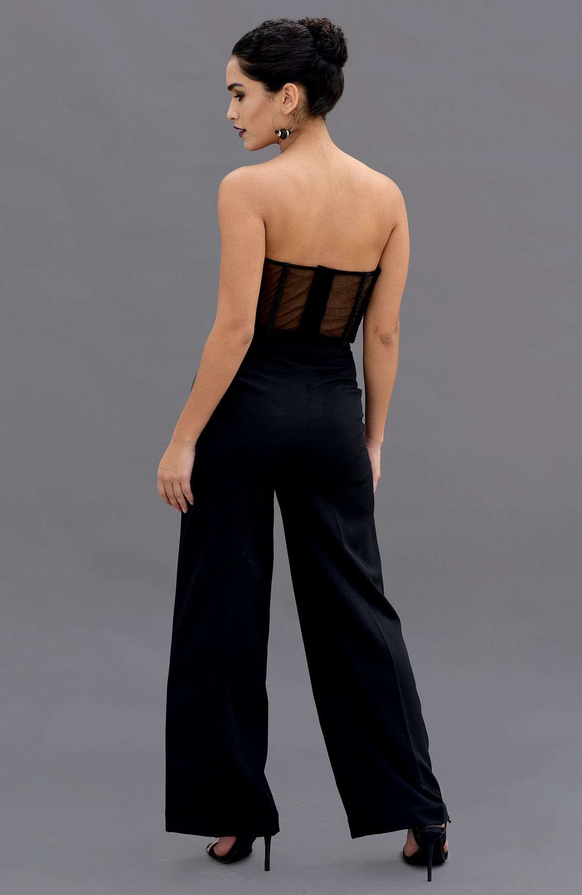A woman models a black hand-embroidered corset and pants set from behind.