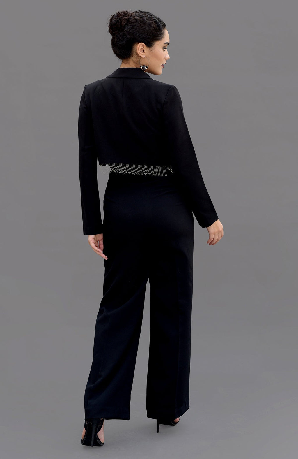 A woman in a black hand-embroidered corset and pants set, viewed from the back.