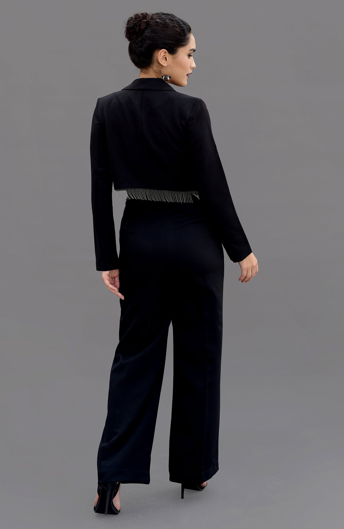 A woman in a black hand-embroidered corset and pants set, viewed from the back.