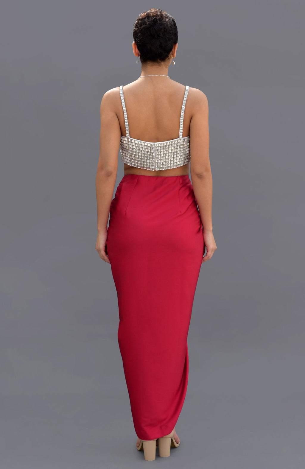 A woman from behind wears a crystal-embroidered bustier and a red draped skirt.
