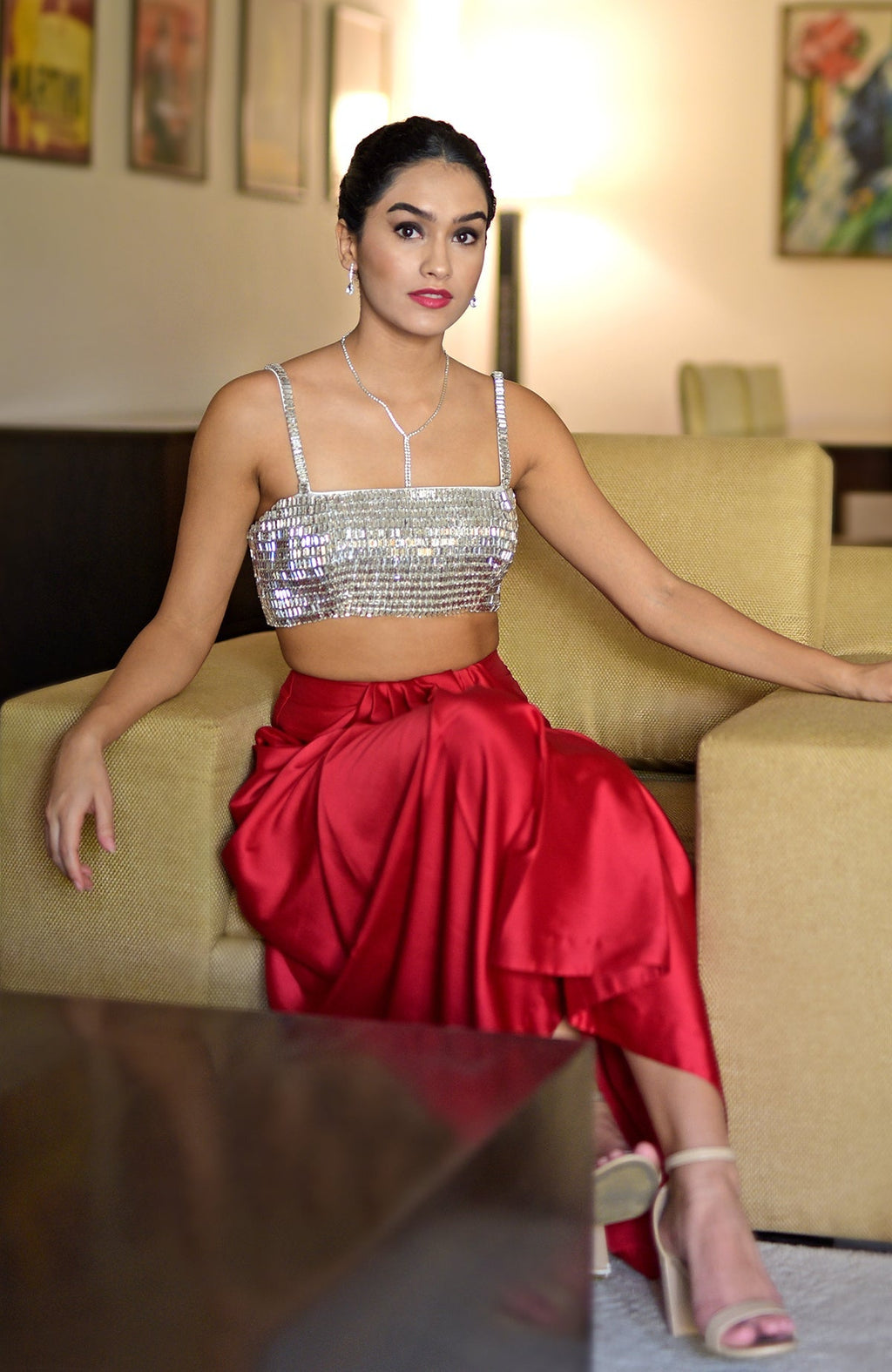 A woman models a crystal-embroidered bustier and a red draped skirt.
