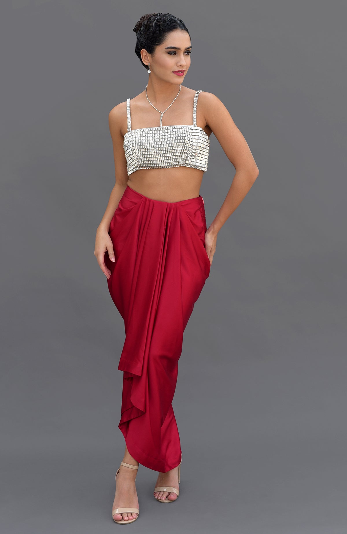 A woman models a diamante crystal hand-embroidered bustier and a red draped skirt.