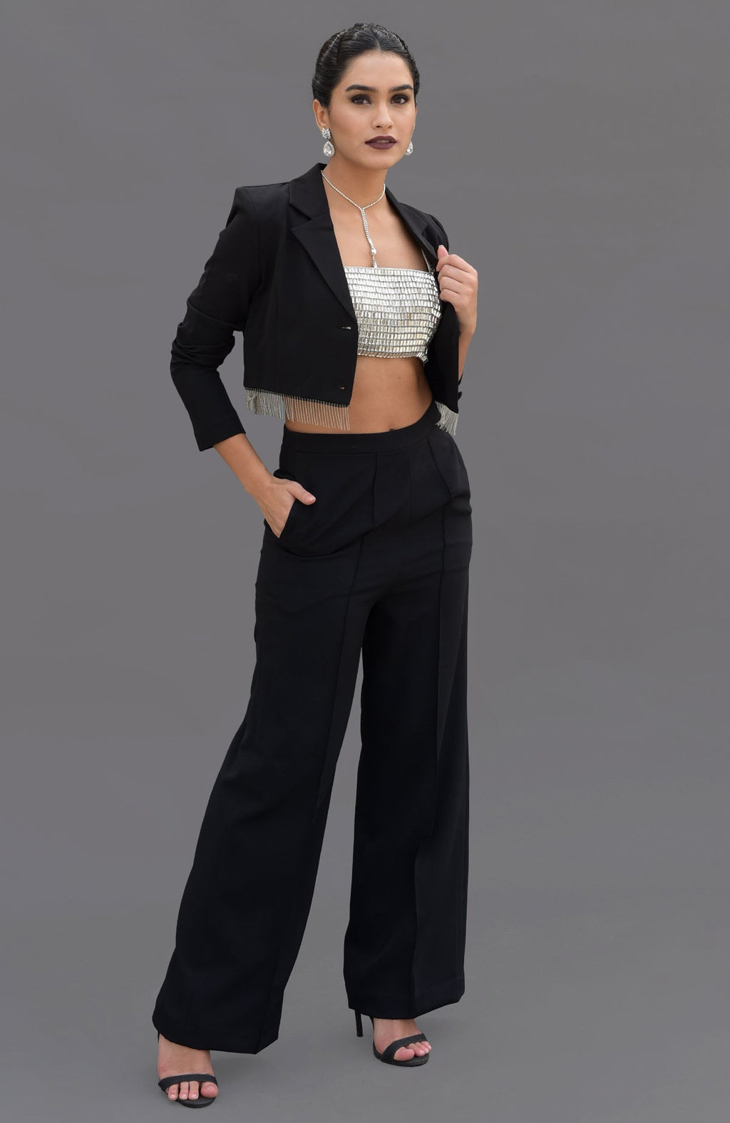 A woman models a black blazer with fringe, a silver bustier, and black pants.