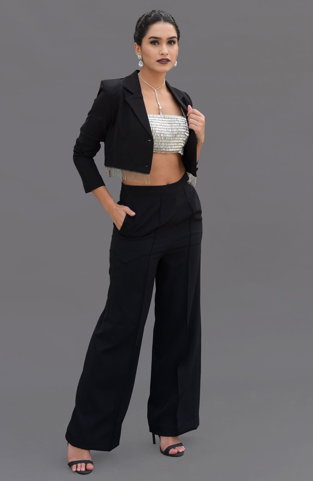 A woman models a black blazer with fringe, a silver bustier, and black pants.