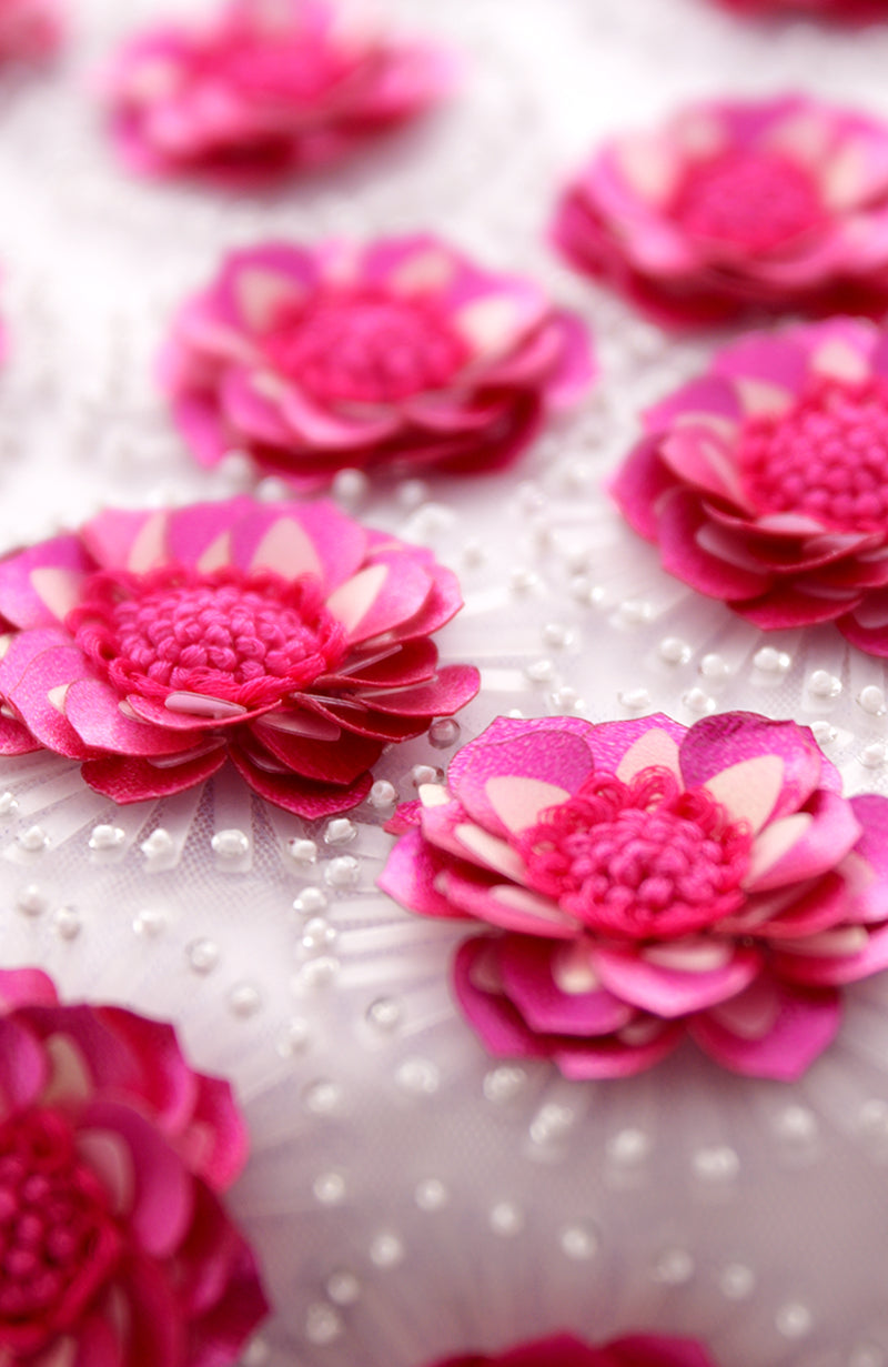 Close-up of fuchsia floral embellishments with white beads on a white fabric.