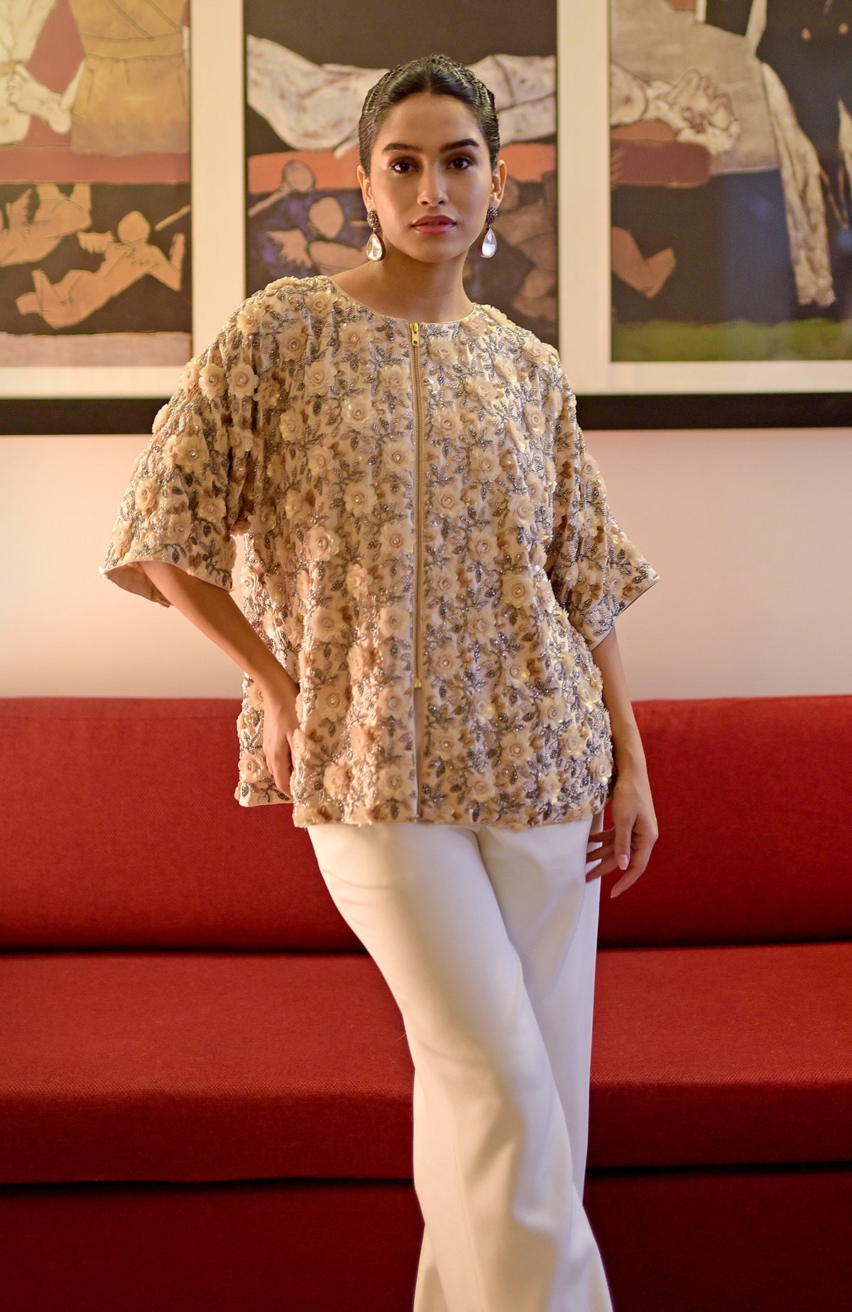 A woman models a light peach hand-embroidered jacket with white pants.