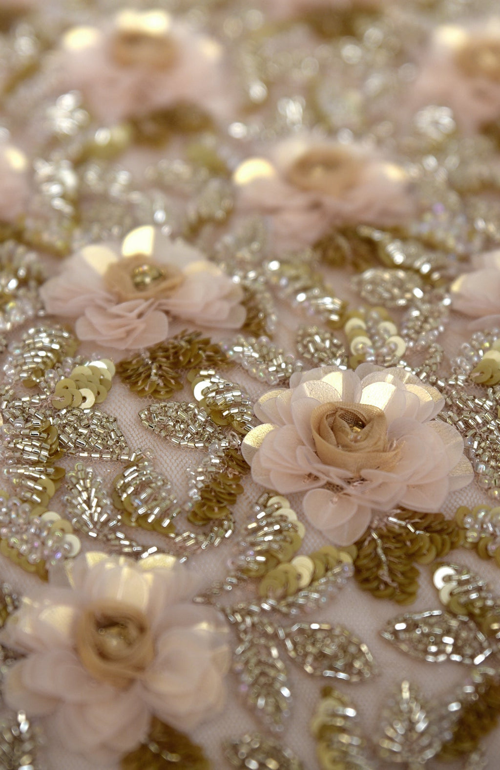 Close-up of light peach fabric with gold sequins, beads, and 3D flowers.