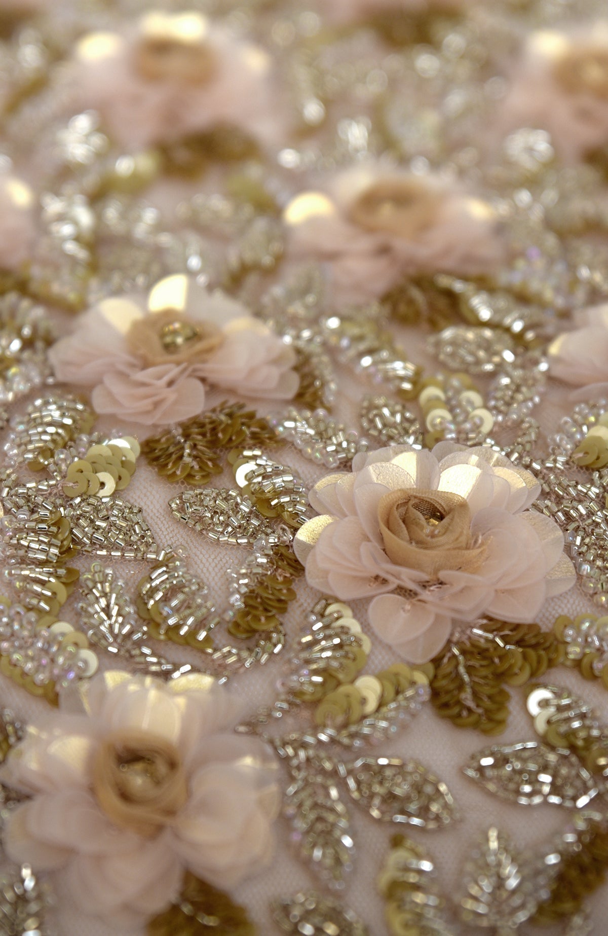 Close-up of light peach fabric with gold sequins, beads, and 3D flowers.