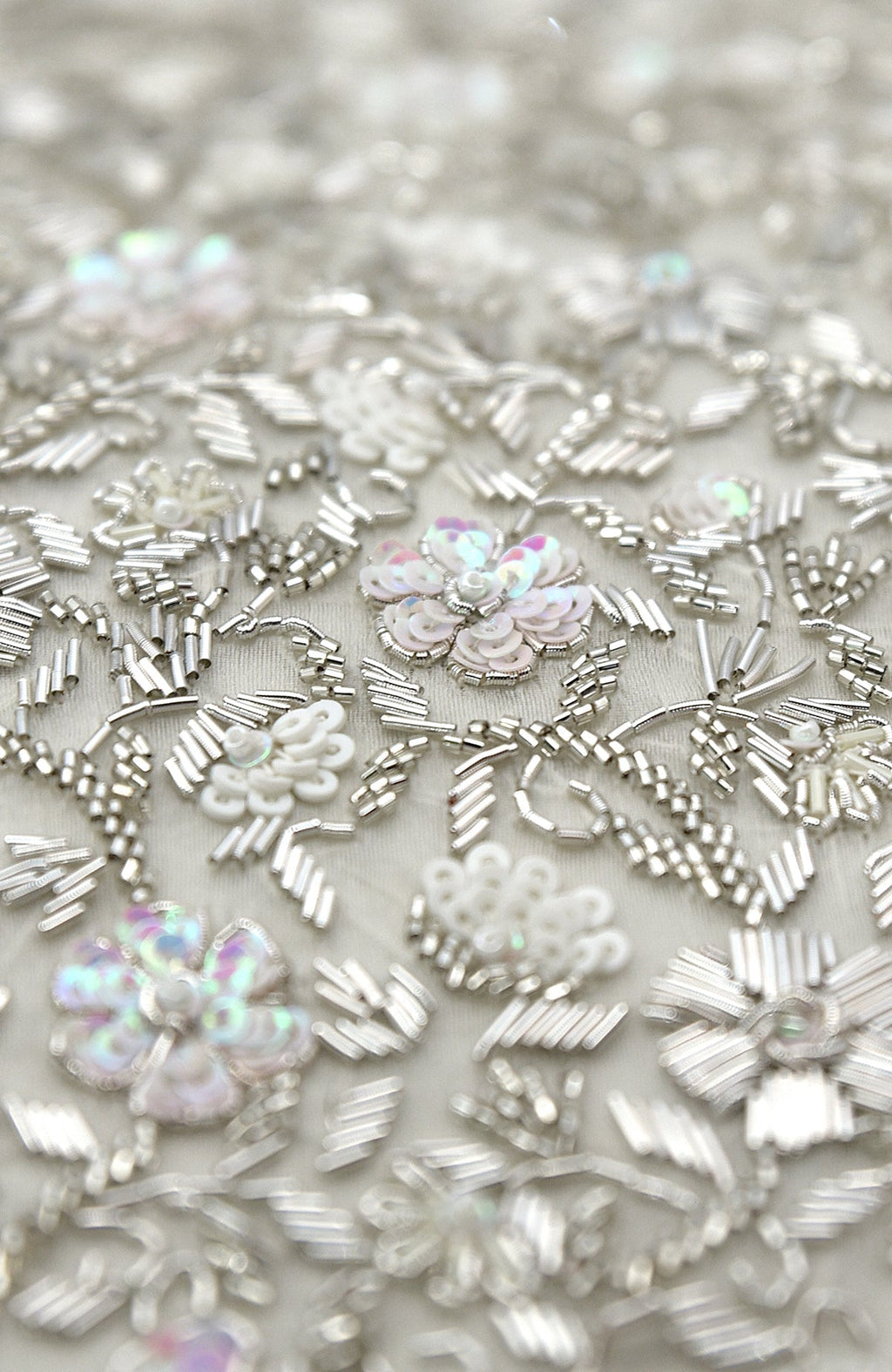 Close-up of white and silver hand embroidery with sequins and beads on fabric.