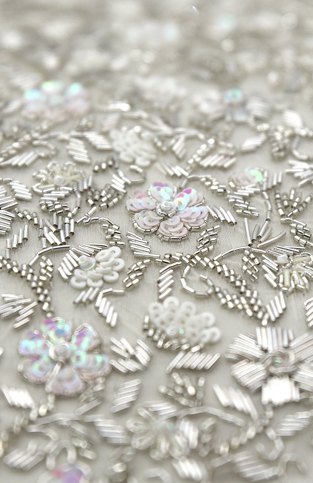 Close-up of white and silver hand embroidery with sequins and beads on fabric.