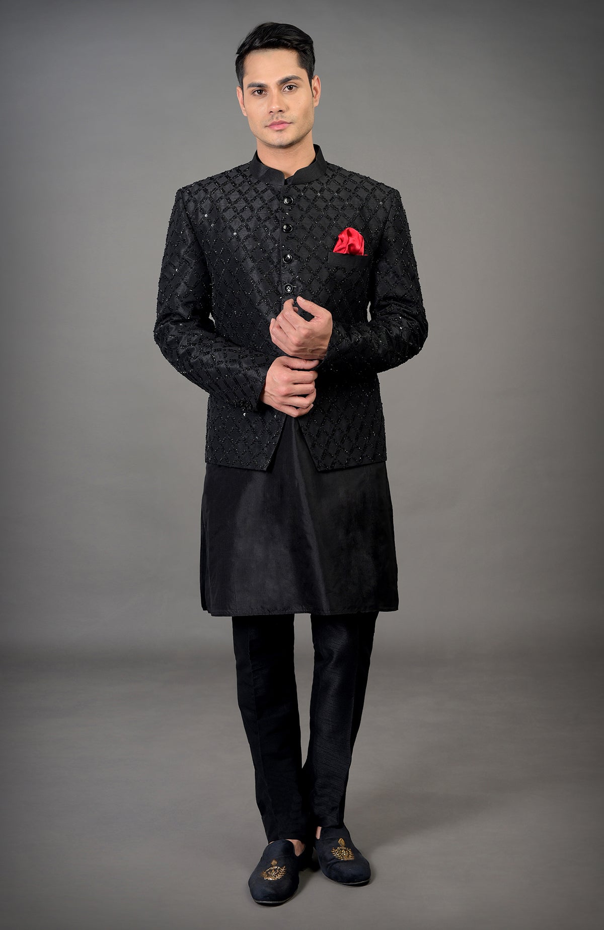 A man models a black chikankari embellished bandhgala jacket set with a red pocket square.