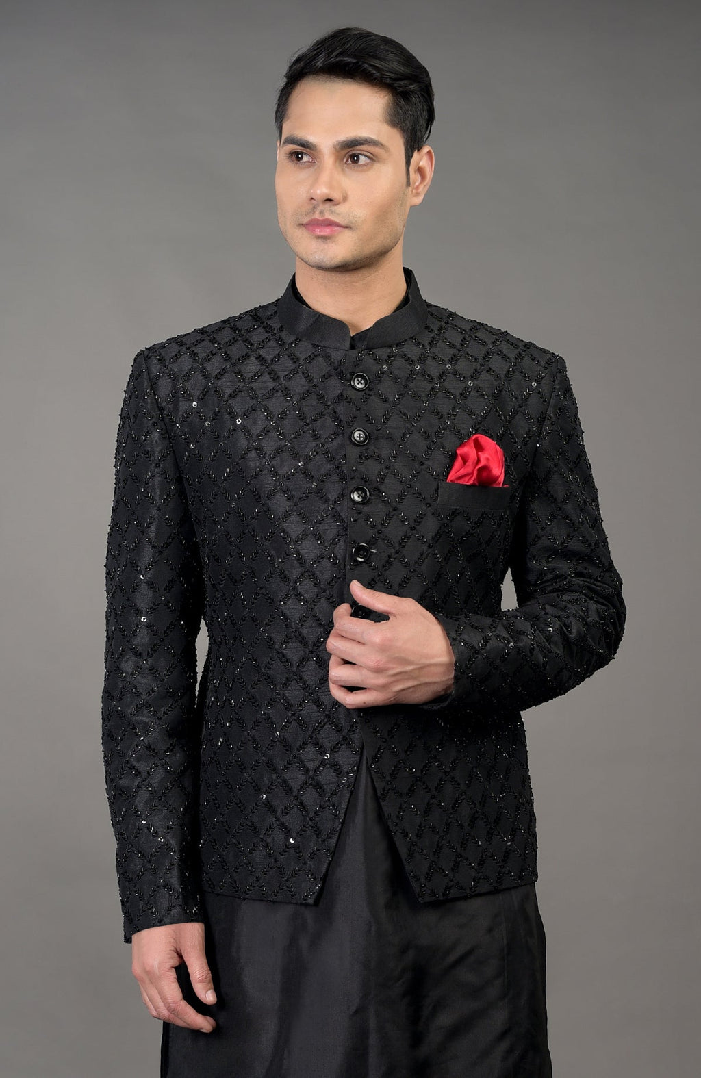 A man models a black chikankari embellished bandhgala jacket set with a red pocket square.