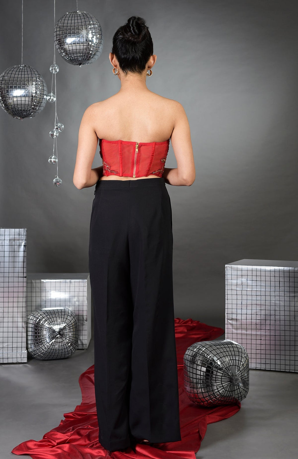 A woman from behind wears a red floral embroidered corset and black wide-legged pants.