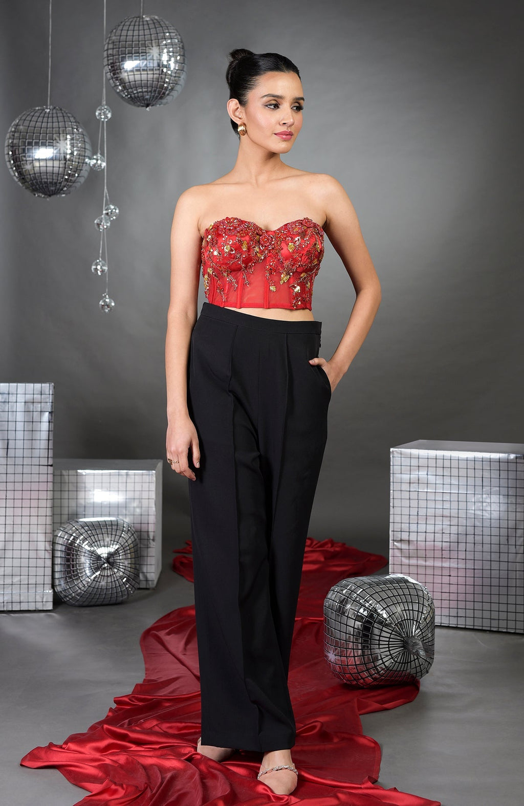 A woman models a red floral embroidered corset with black wide-legged pants.