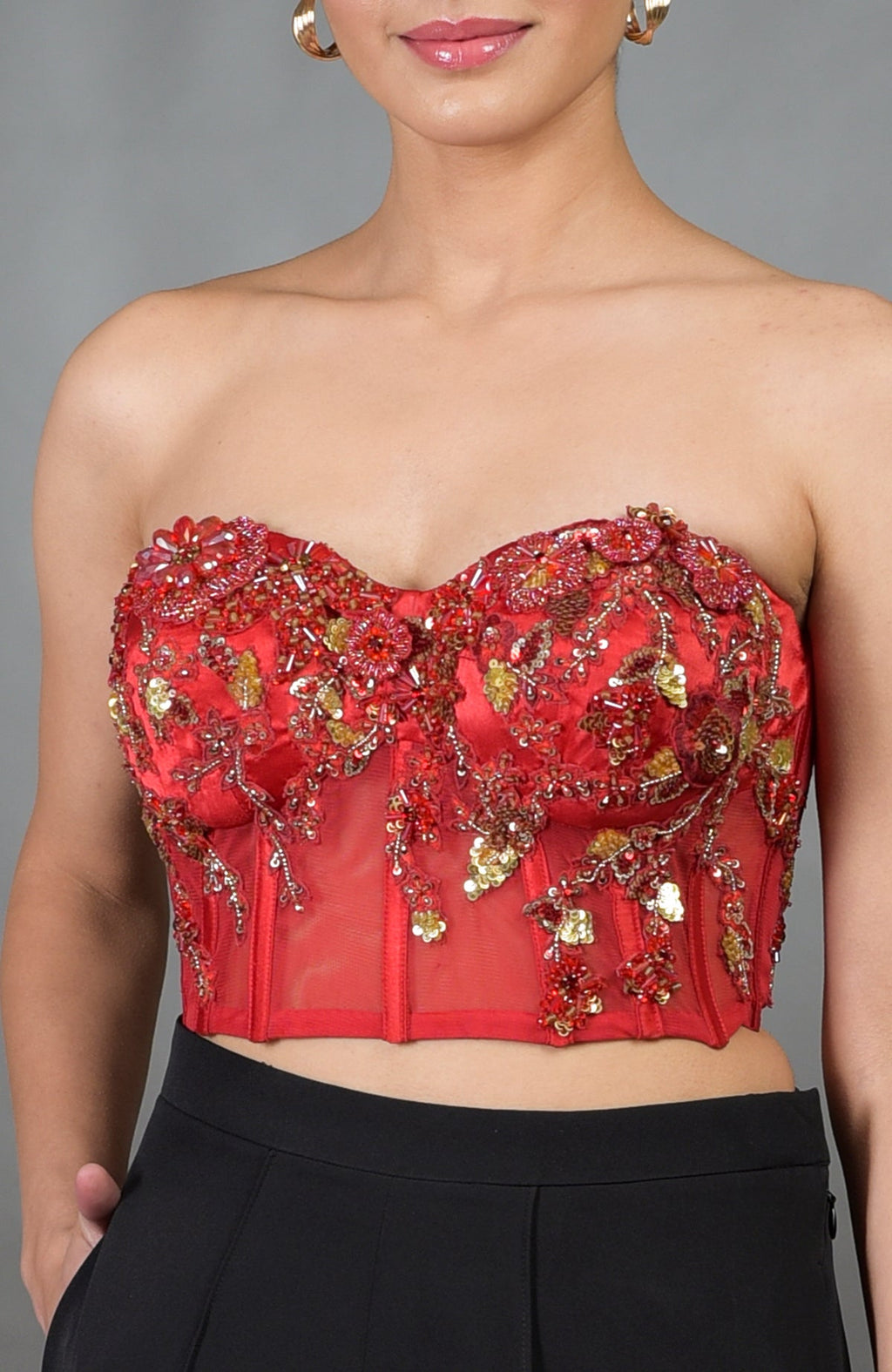 A woman wears a red floral embroidered corset with black wide-legged pants.
