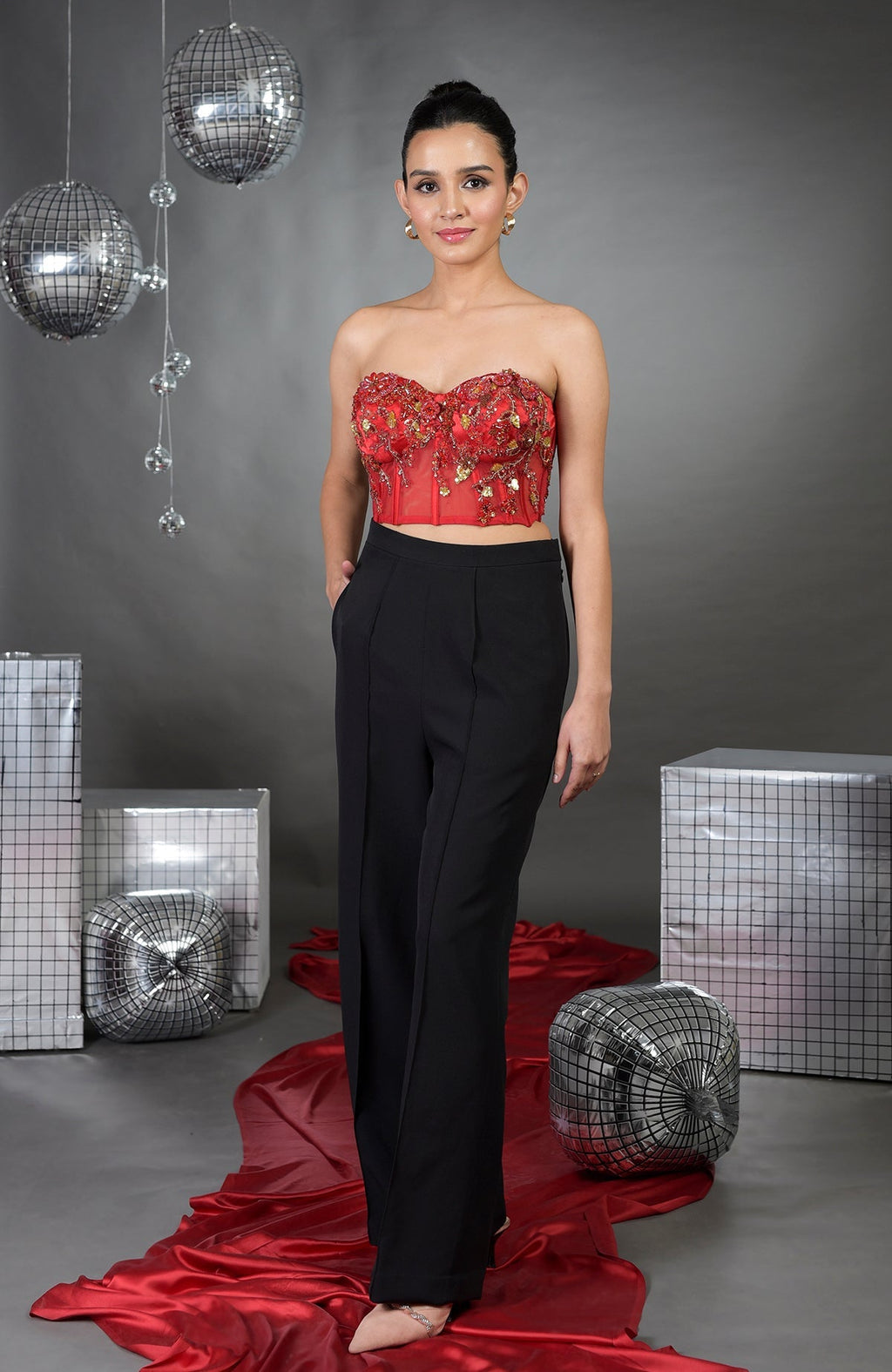 A woman models a red floral embroidered corset with black wide-legged pants.