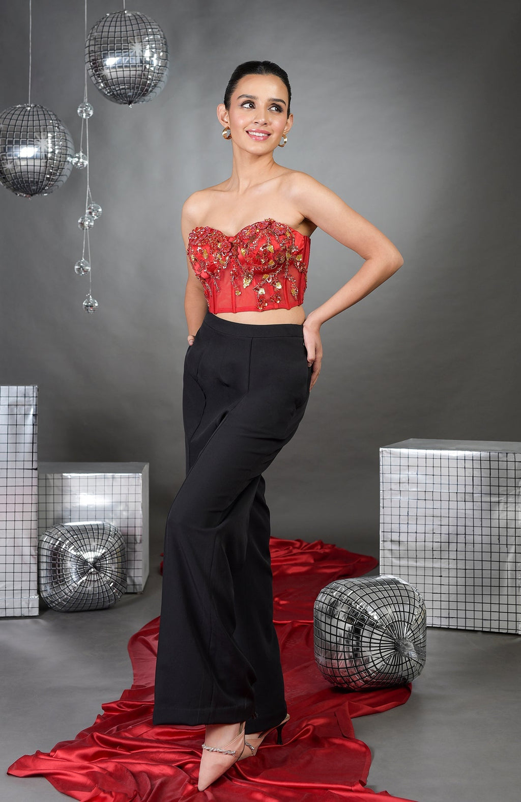 A woman models a red floral embroidered corset with black wide-legged pants.