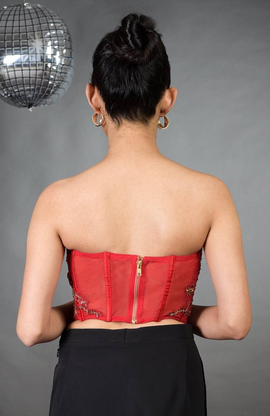 A woman from behind wears a red floral embroidered corset and black pants.