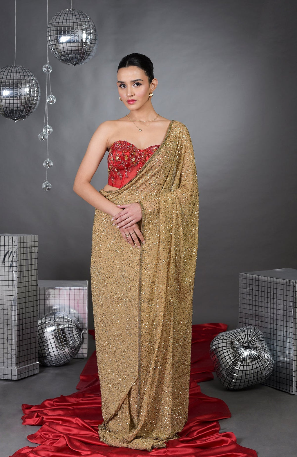 A woman models a gold sequin saree with a red floral embroidered corset.