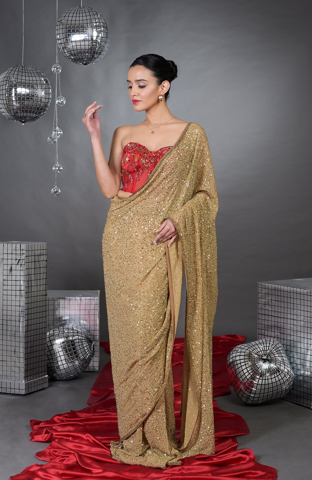 A woman models a gold sequin saree with a red floral embroidered corset.