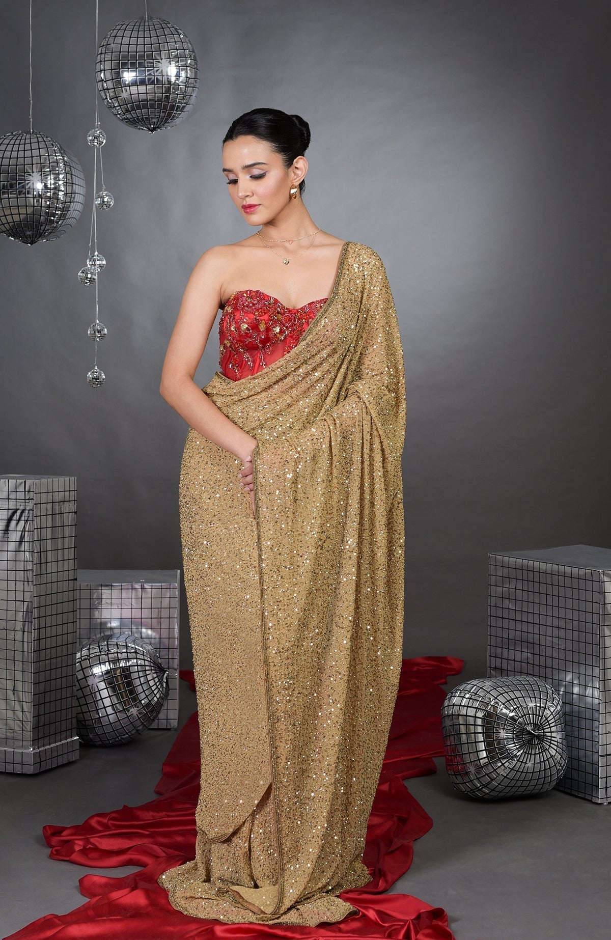 A woman models a gold sequin saree with a red floral embroidered corset.