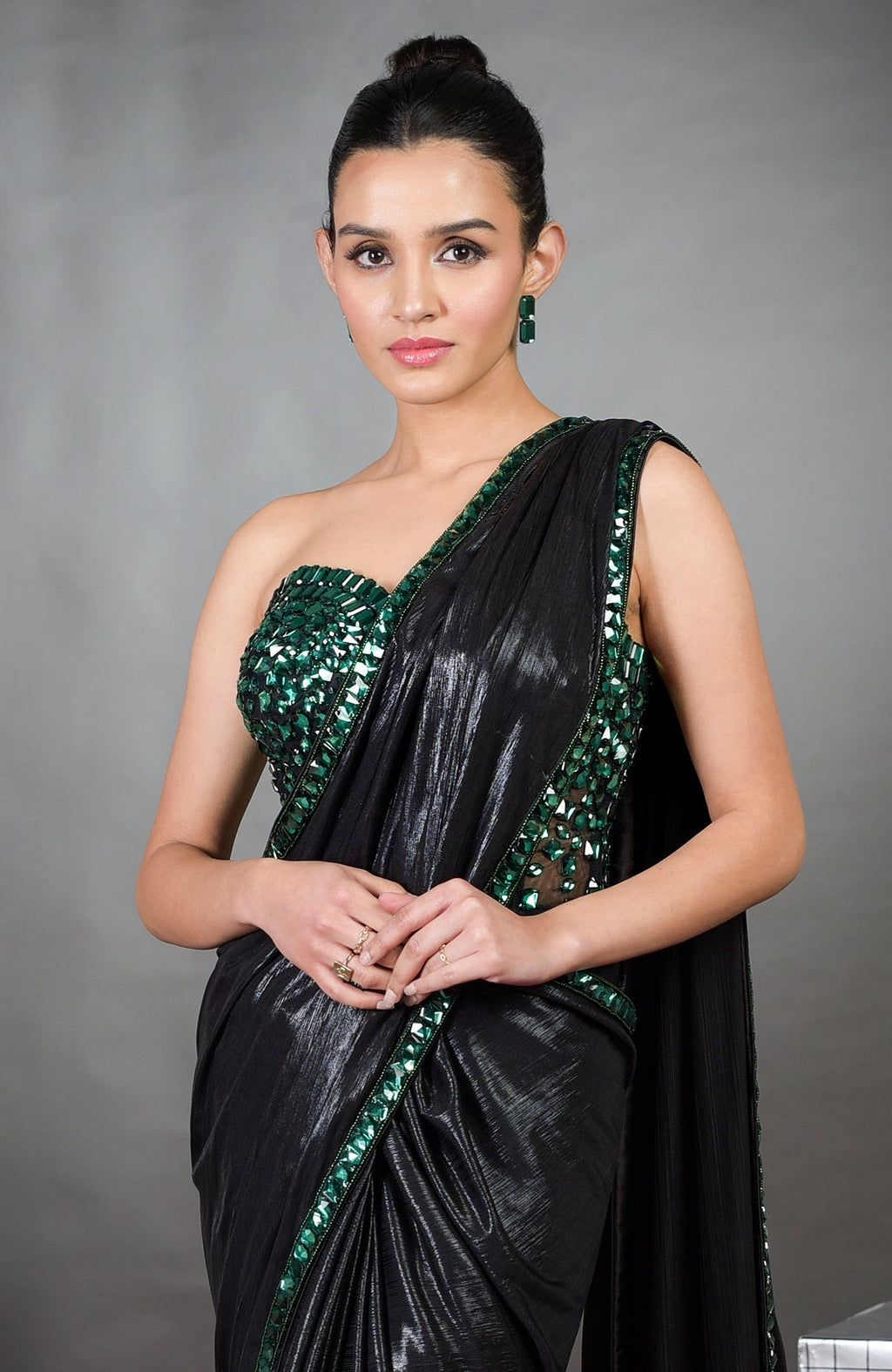 A woman models a black saree with an emerald green embroidered corset and matching earrings.
